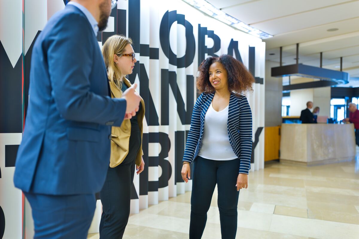 Two women and a man talking in a building lobby