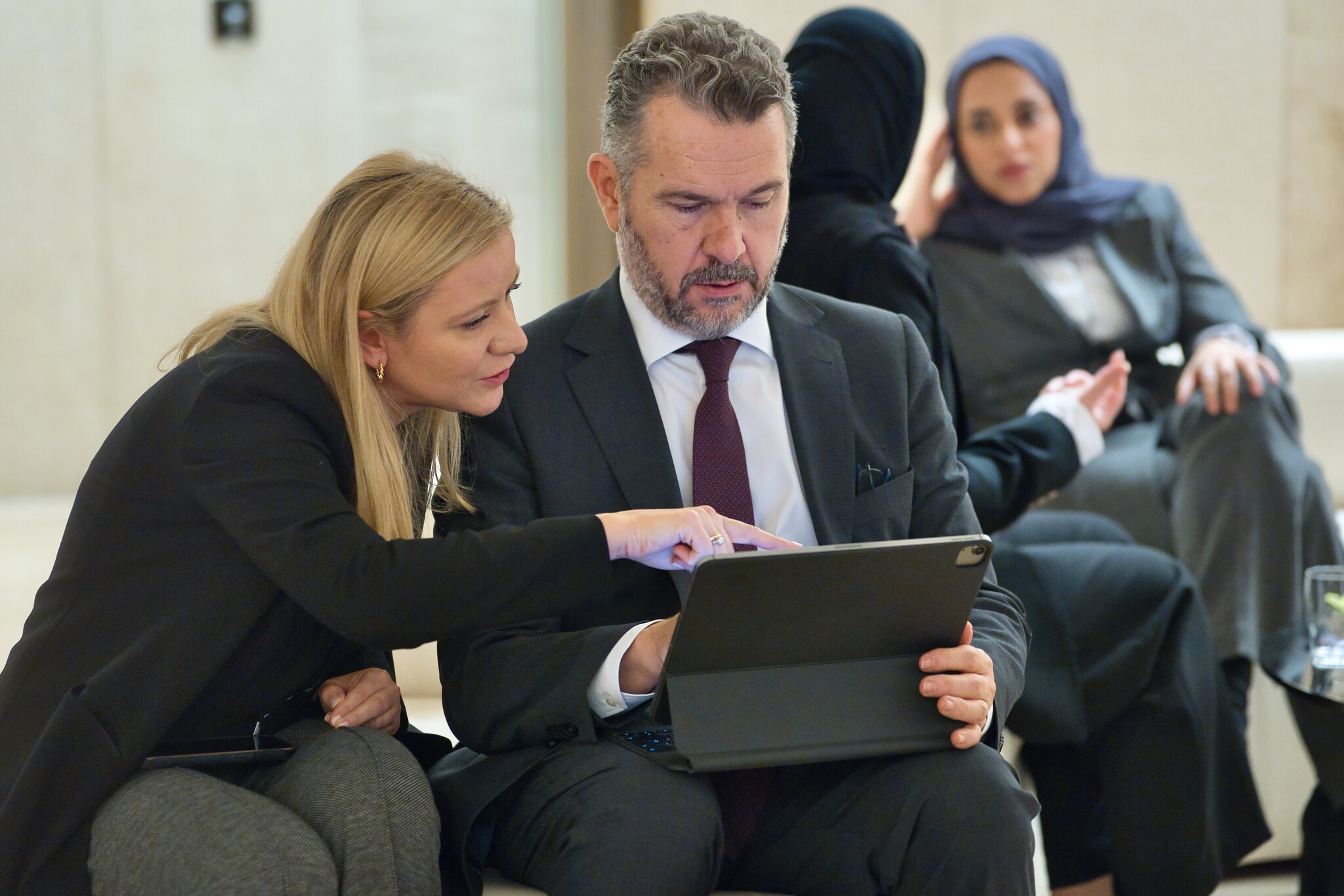 A man and a woman sitting, while looking at a tablet