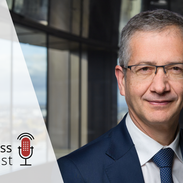 Pablo Hernandez de Cos in a suit and glasses standing in an office setting with large windows in the background. The text 'BISness podcast' with a red microphone icon is displayed on the left, representing a podcast theme.