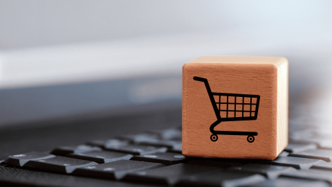 Wooden cube with a black shopping cart icon placed on a computer keyboard, symbolizing e-commerce or online shopping.