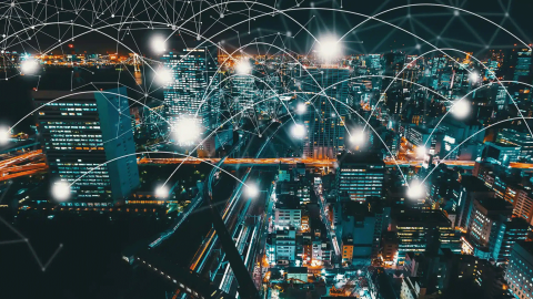 Nighttime cityscape with illuminated buildings and a network of glowing nodes and connecting lines, symbolizing digital connectivity and smart city technology
