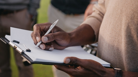 cropped view of african american man writing something on paper in clipboard